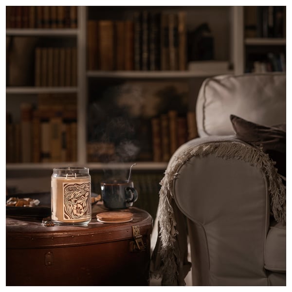 Cozy interior: beige chair, lit candle, mug, bookshelf.