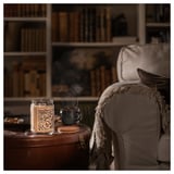 Cozy interior: beige chair, lit candle, mug, bookshelf.