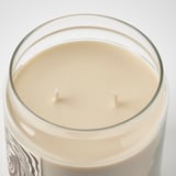 Close-up of elegant glass candle with dual cotton wicks, smooth vanilla wax, white label, on white surface.