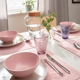 A table set with colorful pink bowls, swirled glasses, and metal cutlery, accented by a textured glass vase with flowers.