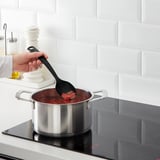 Hand stirring red liquid on stove with black spoon.