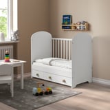 Nursery with white GONATT cot, wooden drawers, grey rug, and toys. Cot has high sides, a drawer, and is smaller than typical furniture.