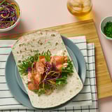 A flatbread wrap with salmon, greens, and sauce on a green plate. Surrounded by bowls of salad and herbs.