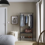 GRÅFJÄLLET black clothes rack with hanging rods and shelves by bed and window.