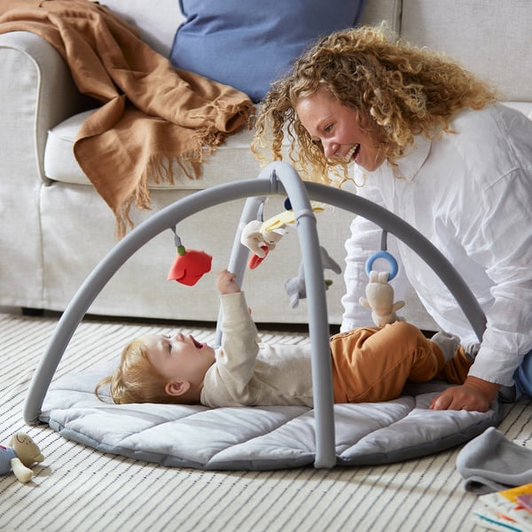 Woman with baby on GULLIGAST gym. Baby reaches for toys, mirror promotes coordination.