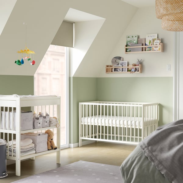 A nursery with a white GULLIVER cot and changing table, light green wall, and a mobile with toys.