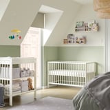 A nursery with a white GULLIVER cot and changing table, light green wall, and a mobile with toys.