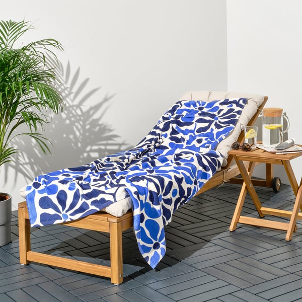 Blue and white floral GULYXNE towel on wooden lounge chair with pillow and side table.