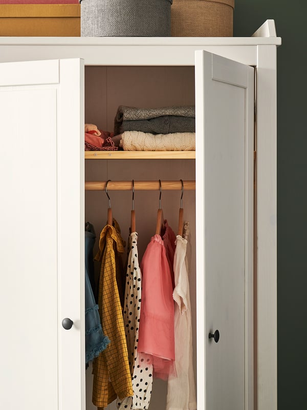 White wooden wardrobe with childrens clothes and hangers, neatly organized.