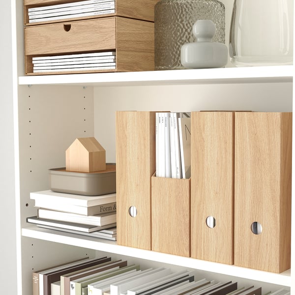 White bookshelf with wooden magazine files storing papers and books. Decorative items on top.