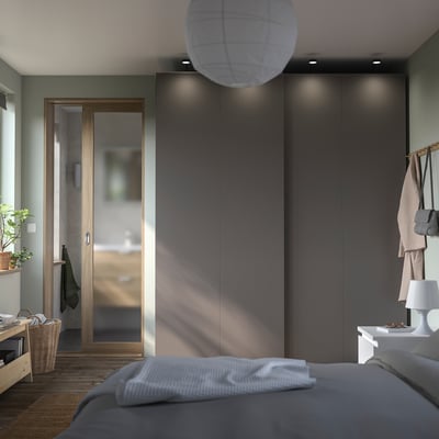 Bedroom with grey bed, grey HASVIK door, hanging lamp, wooden coat rack, wicker basket, and a grey blanket.
