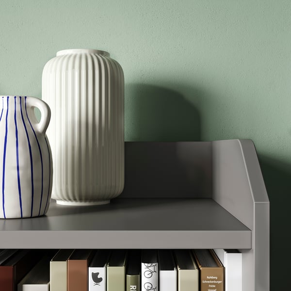 Modern shelf with sleek grey top, holding 2 white vases and books against a green wall.