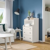 Modern room with white HAUGA chest, blue wall, plants, white curtains, and white furniture.