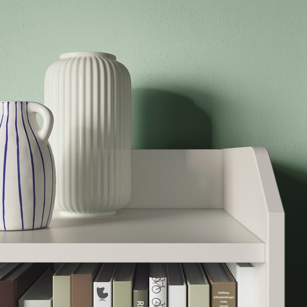 Modern white shelf with books and vases, green wall.