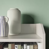 Modern white shelf with books and vases, green wall.