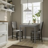 Compact dining set with gray table & matching chairs near window, white shelves, light wood floors.