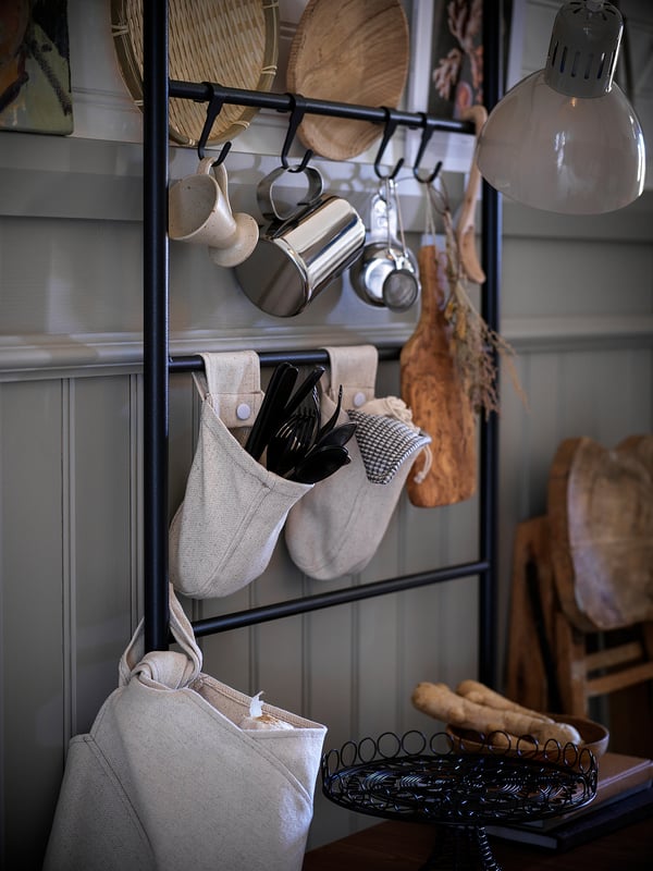 Modern kitchen setup with a metal storage rack holding pots, utensils, and woven baskets. Includes a hanging lamp and wooden furniture.