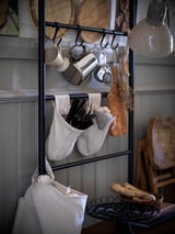 Modern kitchen setup with a metal storage rack holding pots, utensils, and woven baskets. Includes a hanging lamp and wooden furniture.
