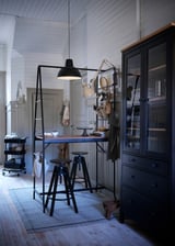 Black metal-framed kitchen table with two stools, modern design, hanging storage, and a large pendant light.