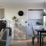 Modern living room featuring a rustic gray HAVSTA cabinet, a black wall clock, cushioned chairs, and wooden floors.