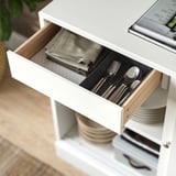 Open white wooden drawer revealing neatly organized cutlery and folded napkins.