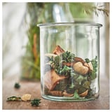 Clear glass jar with green and brown dried plants inside, sitting on a wooden surface.