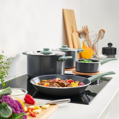 Green HEMLAGAD cookware on stove with vegetables.