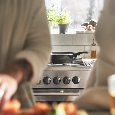 Stainless steel stove with non-stick pan, black handle, and knobs, cooking food with steam rising.