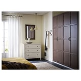 A modern bedroom with white dresser, mirror, yellow lights, and dark wooden closet.