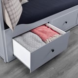 Open white bed drawer revealing folded blankets, demonstrating storage function.