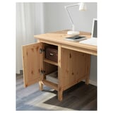 Wooden desk with open door showing storage. A lamp, laptop, and notebook are on the desk.