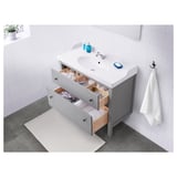 Bathroom vanity with open drawers showing organized toiletries and towels, sink with faucet, and blue toiletries on countertop.