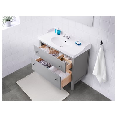 Bathroom vanity with open drawers showing toiletries, sink, and towel.