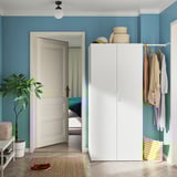 A tidy blue room with a white HJÄLPA storage unit. The unit has baskets, clothes on hangers, and a plant beside it.