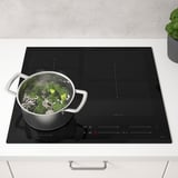 Kitchen with black induction stove cooking veggies, steam rises.