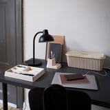 Minimalist workspace with black desk, chair, and cable management box. Clutter-free with office supplies and lamp.