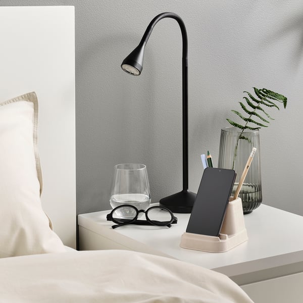 Bedside setup with lamp, phone stand, glasses, cup, and plant.