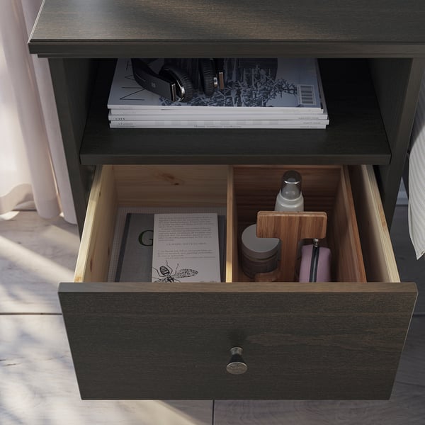 Dark wooden bedside table with drawer and shelf. Drawer holds book, tissues, and pens.