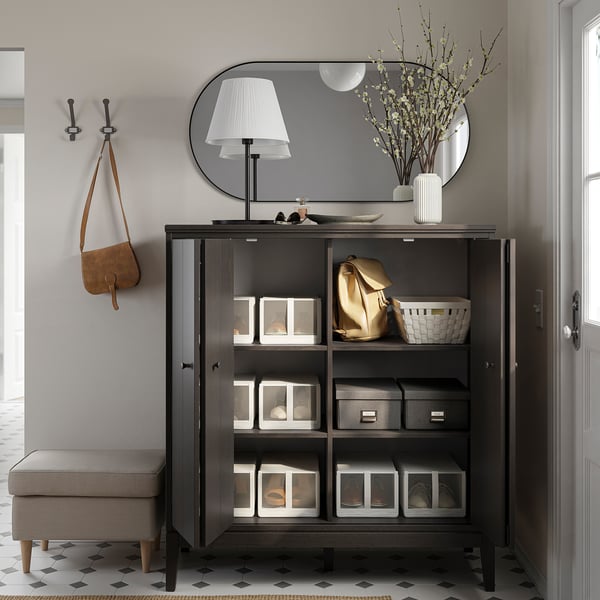 Modern entryway setup with IDANÄS black cabinet, mirror, lamp, and hooks. Includes organized storage with clear boxes and a bench.