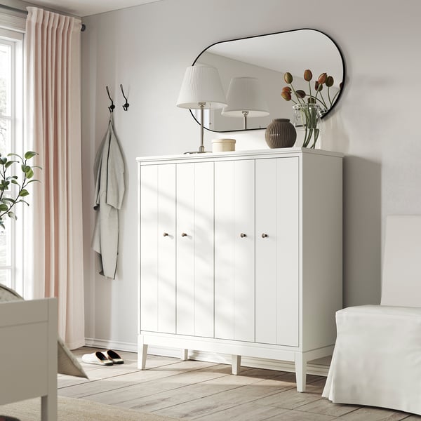 Modern entryway with white IDANÄS cabinet, mirror, lamps, flowers, coat hooks, and light pink curtains.