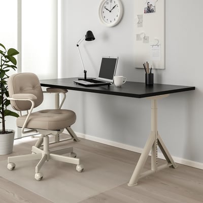 Black IDÅSEN desk with adjustable underframe and cable management, paired with beige swivel chair. Modern and minimalist design.
