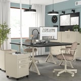 Modern home office with IDÅSEN beige desk, adjustable height, and cable management. Beige chair, cream cabinetry, light blue walls, & stapler lamp.