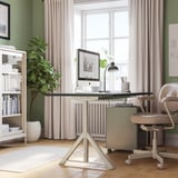 Clean home office with IDÅSEN desk, cream-colored, wooden floor, green walls, large window, white rug, potted plant, and office chair.