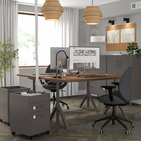 Office with IDÅSEN desks, black chairs, two monitors each. Grey cabinets, natural & pendant lighting, corkboard.