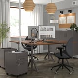 Office with IDÅSEN desks, black chairs, two monitors each. Grey cabinets, natural & pendant lighting, corkboard.