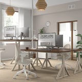 Modern office with IDÅSEN desks, chairs, monitors, lights, clock, window, plant.