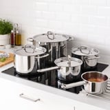 A set of IKEA 365+ stainless steel pots and pans on a black stovetop. Pots have lids and are used for cooking various foods.