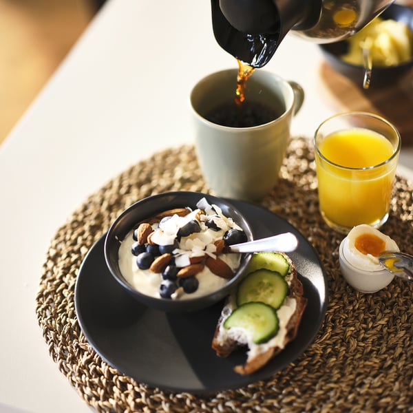 Breakfast setup: coffee pouring, yogurt bowl with berries, almonds, toast with cucumber, and orange juice.