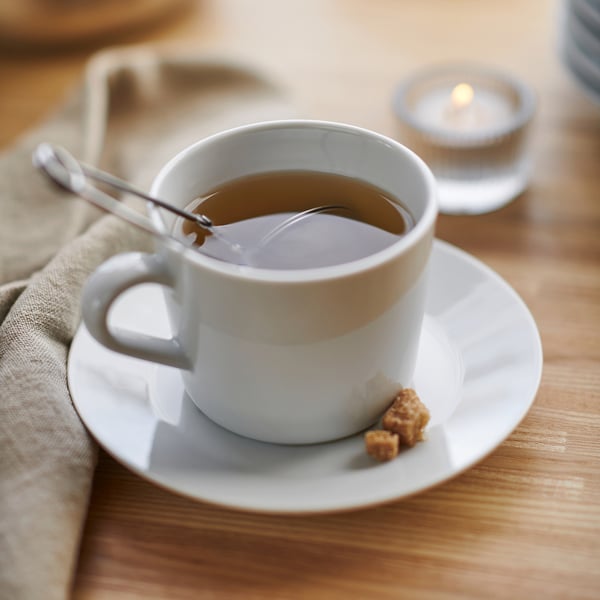 Cup of tea on white porcelain, with a spoon and sugar cube, placed on a wooden table.
