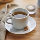 Cup of tea on white porcelain, with a spoon and sugar cube, placed on a wooden table.